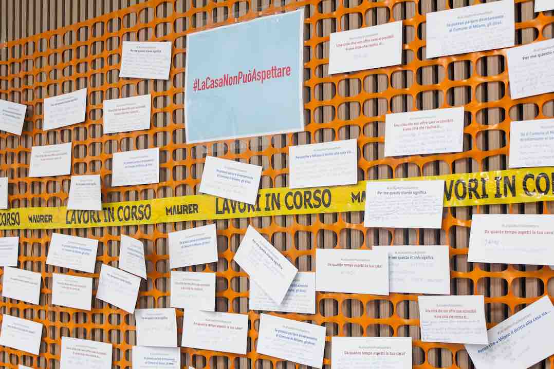 Installazione simbolica in via della Signora a Milano, con biglietti appesi a una rete da cantiere, raccoglie le voci di chi attende casa